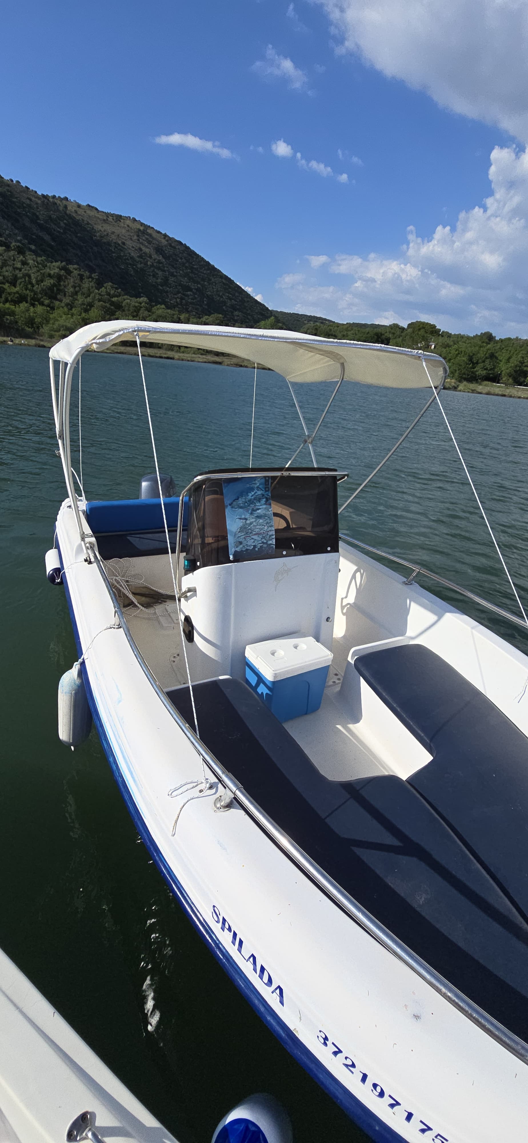 Center console of the Spilada 30HP rental boat featuring easy-to-use steering, blue cushioned seats, a sun tent, and a provided cooler near Ksamil