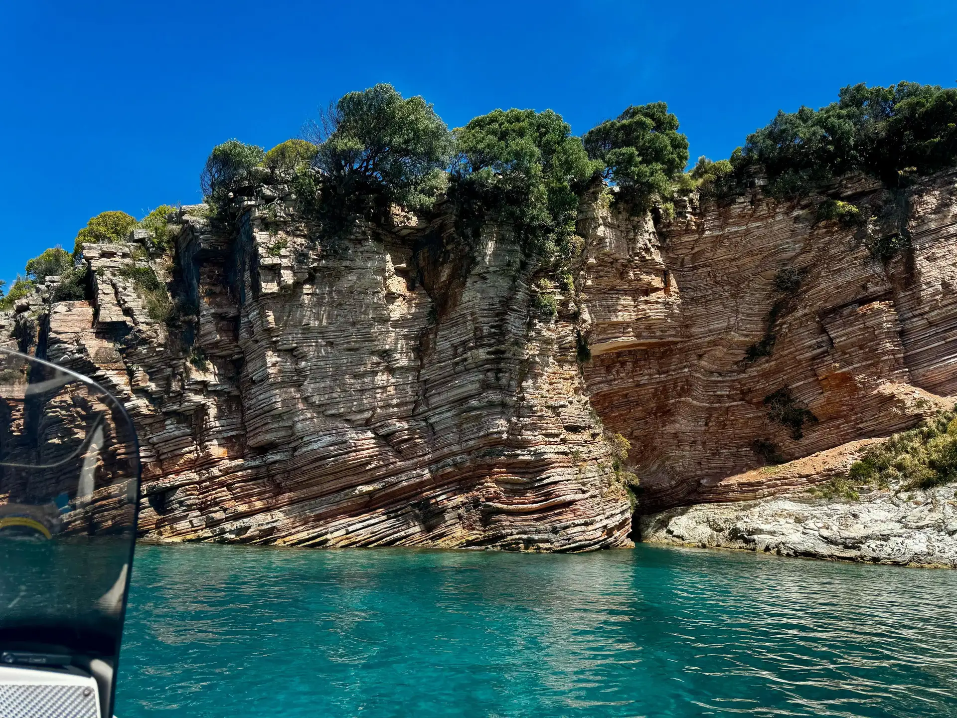 Stunning geological layered cliffs rising from crystal-clear turquoise waters along the rugged coastline near Pigeon Cave