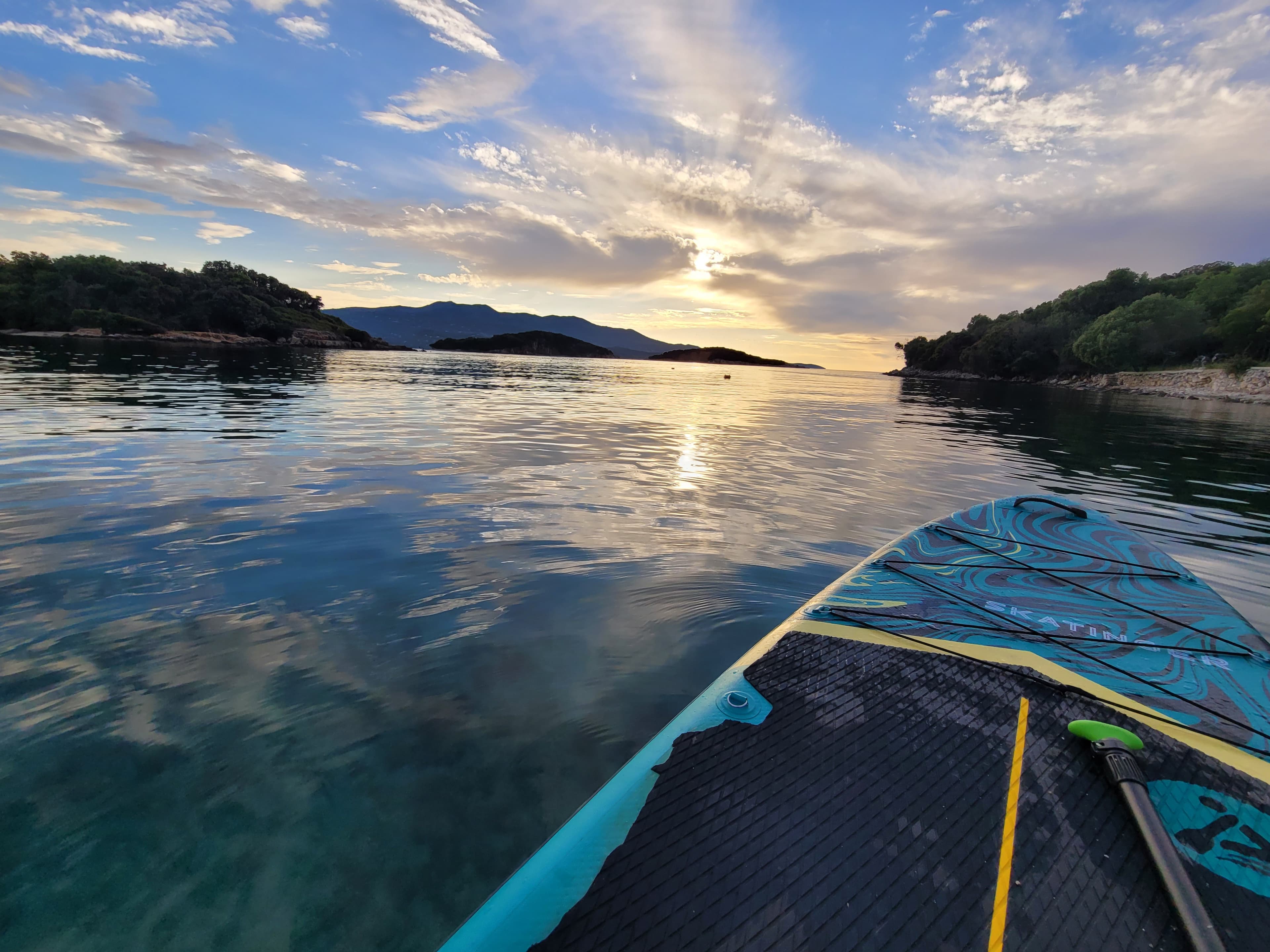 A line of guided SUP tourists paddling on glassy, pristine Ionian Sea waters toward a secluded island in Albania