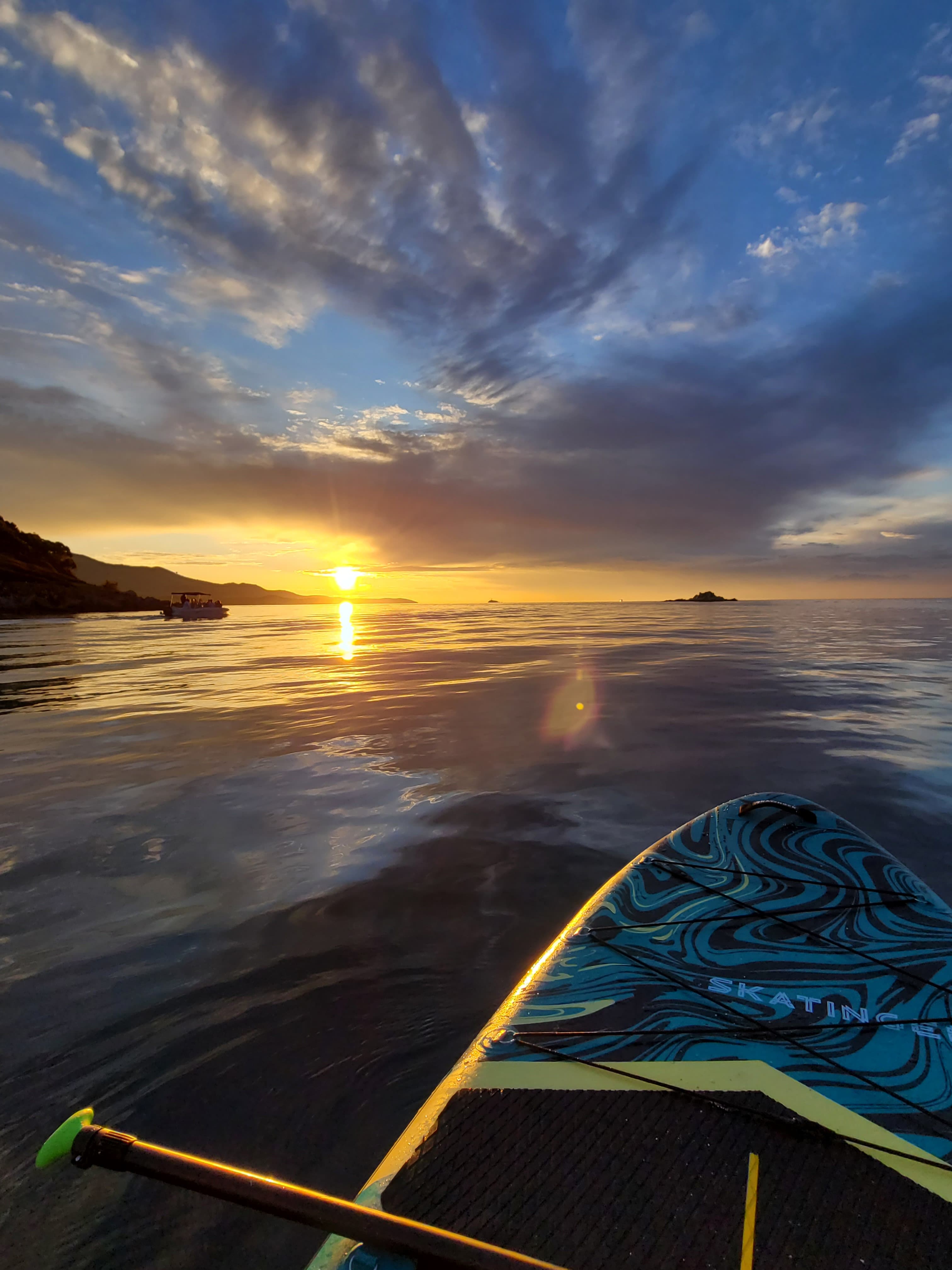 A guided Sunset SUP tour group paddling towards a distant Ksamil island on calm water bathed in warm golden hour light
