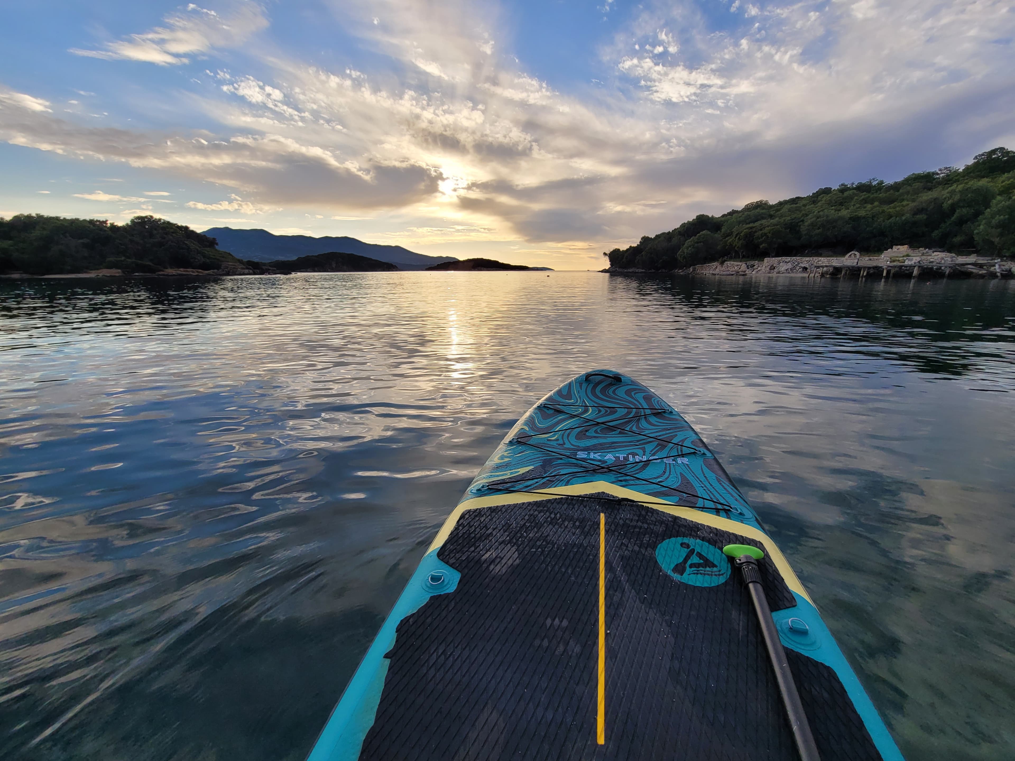 View from inside a Ksamil hidden sea cave looking out at paddleboarders on calm water under dramatic golden sunset light